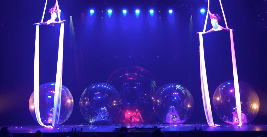 Image du spectacle Rêve de la compagnie Remue-ménage, montrant deux circassiennes pratiquant les tissus aériens et des danseuses évoluant dans des bulles