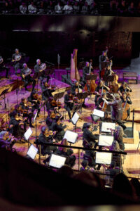 L'orchestre symphonique Divertimento sur scène, composé de musiciens et musiciennes jouant des cordes et des cuivres, dirigé par la cheffe d’orchestre Zahia Ziouni? Photo prise en plongée.